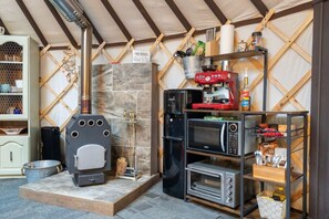 A compact kitchen with a wood stove, a coffee machine, a microwave, and a shelf with utensils.