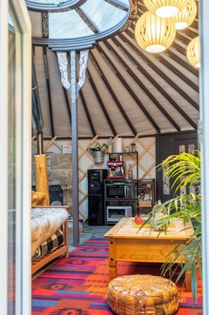 A cozy interior with a curved ceiling, a wooden table, a sofa, and a coffee machine. - `Shanti Yurt` with private hot tub in Bragg Creek (Bragg Creek)