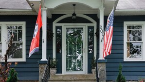 A house with a front porch, a stone foundation, and a flagpole with two flags. - The Bellmore Cottage (Nashville)