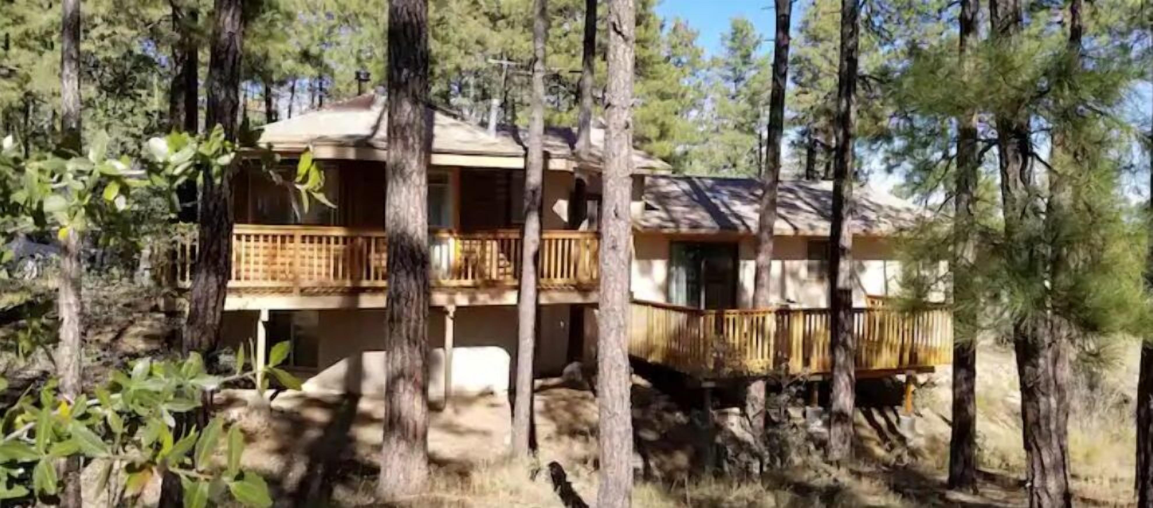 Une cabane à deux étages dotée d’un balcon, entourée de grands pins.
