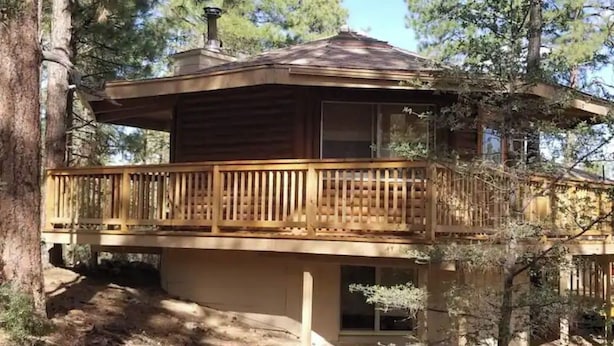 Una cabaña de madera con balcón, rodeada de árboles.