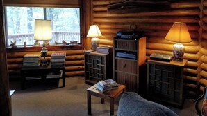 Interior acogedor de una cabaña de madera con chimenea, estanterías y dos lámparas.