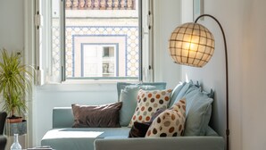 A room with a window, a sofa with patterned cushions, a floor lamp, and a potted plant. - Bright 2BR Baixa Flat w/ Elevator | Balcony, Downtown Views & Full A/C (Lisboa ciudad)