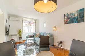 A modern living room with a sofa, chairs, a coffee table, a floor lamp, and a cityscape painting.