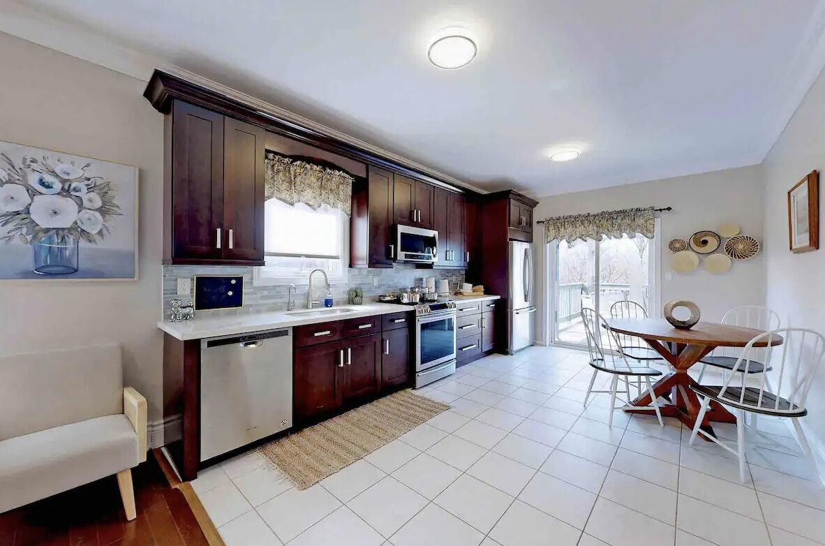 Una cocina moderna con armarios de madera oscura, encimera blanca y un comedor con mesa de madera y sillas blancas.