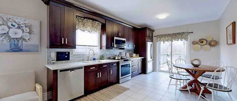 Una cocina moderna con armarios de madera oscura, encimera blanca y un comedor con mesa de madera y sillas blancas.