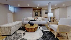 Een moderne woonkamer met een bank, een houten salontafel, een witte fauteuil en een gestreept voetenbankje.