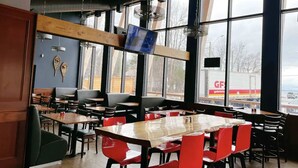 Een restaurantinterieur met grote ramen, houten tafels en rode stoelen.