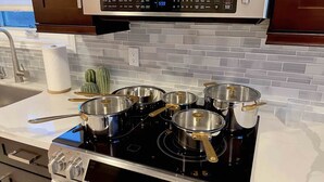 Een keuken met een zwarte kookplaat, vier pannen erop en een magnetron erboven.