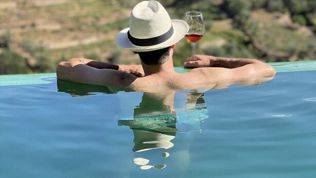 A person relaxing in a clear pool with a drink, surrounded by greenery and hills. - Detached house in the Douro with stunning river and mountain views (Mesão Frio)