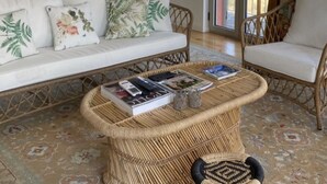 A living room with a sofa, a wicker coffee table, and a chair. There is a fireplace, a large window, and a door leading outside. - Detached house in the Douro with stunning river and mountain views (Mesão Frio)