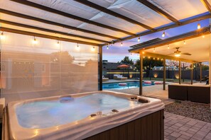 Un bain à remous sous un patio couvert, avec une piscine et un espace salon extérieur.