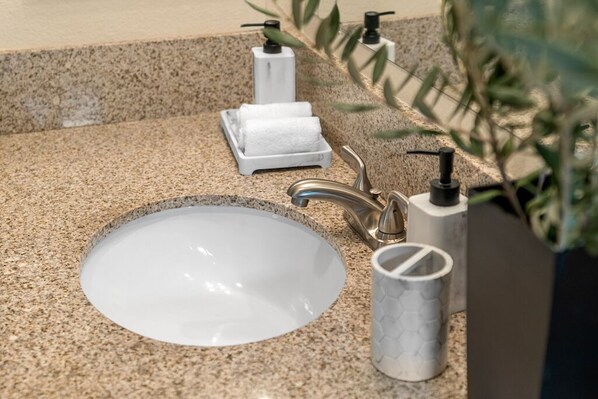 A bathroom sink with a granite countertop, a faucet, and two soap dispensers.