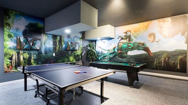 Mesa de bilhar e jogos de sinuca em um espaço com grandes painéis de temática natural.