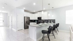 A modern kitchen with white cabinetry, a central island with bar stools, and a black backsplash.