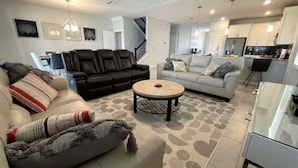 A modern living room with a sofa, a coffee table, and a dining area with a kitchen in the background.