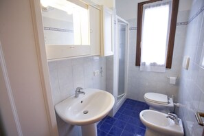 A bathroom with two sinks, a toilet, a shower, and a window with curtains.