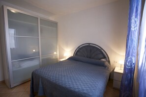 A bedroom with a bed, a wardrobe with frosted glass doors, and two bedside lamps.