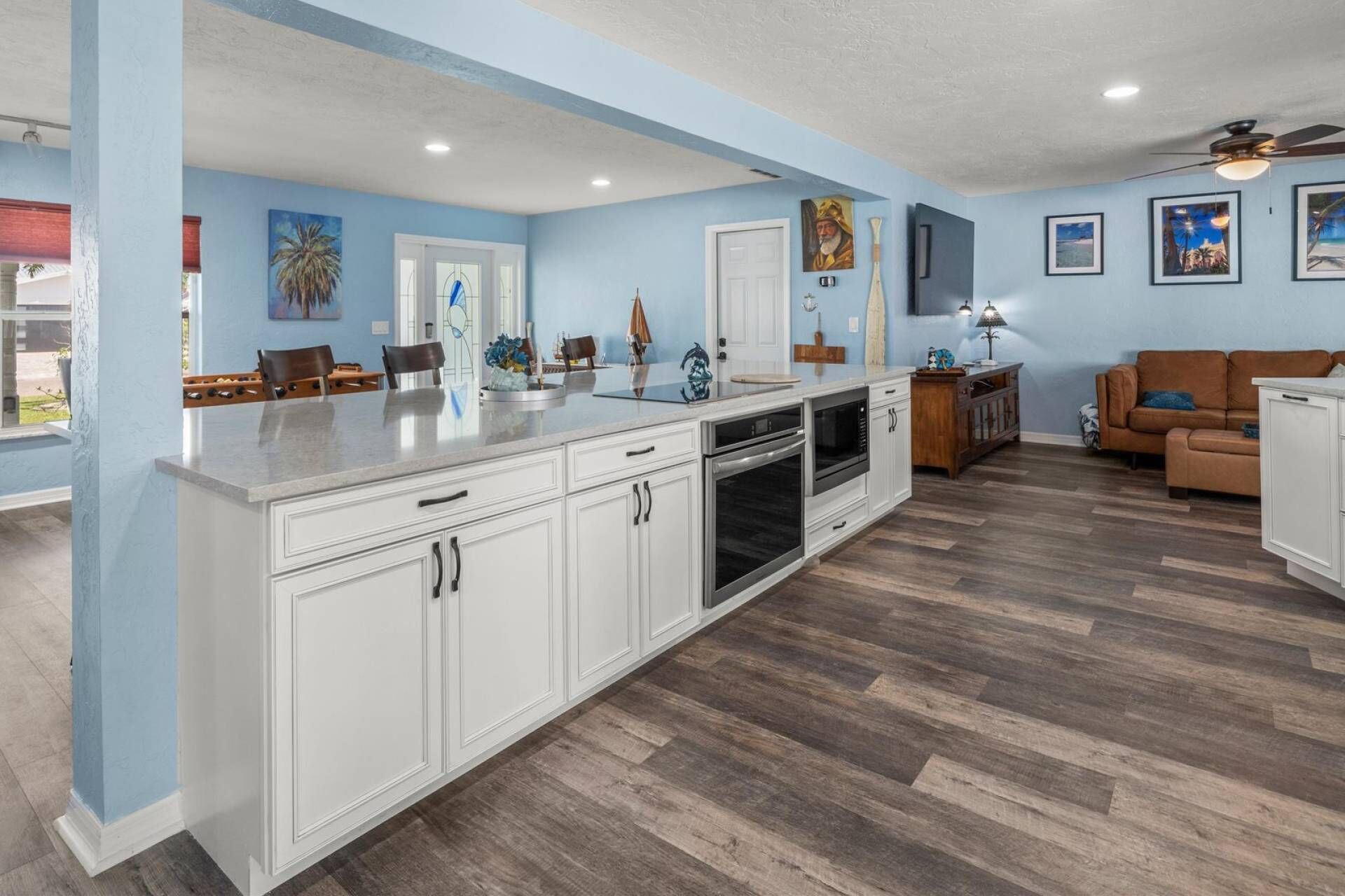 A modern kitchen with white cabinetry, a large island, and a dining area with a brown leather couch.