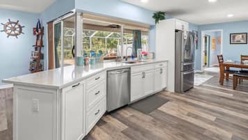 A modern kitchen with white cabinetry, a stainless steel refrigerator, and a large window overlooking a garden.