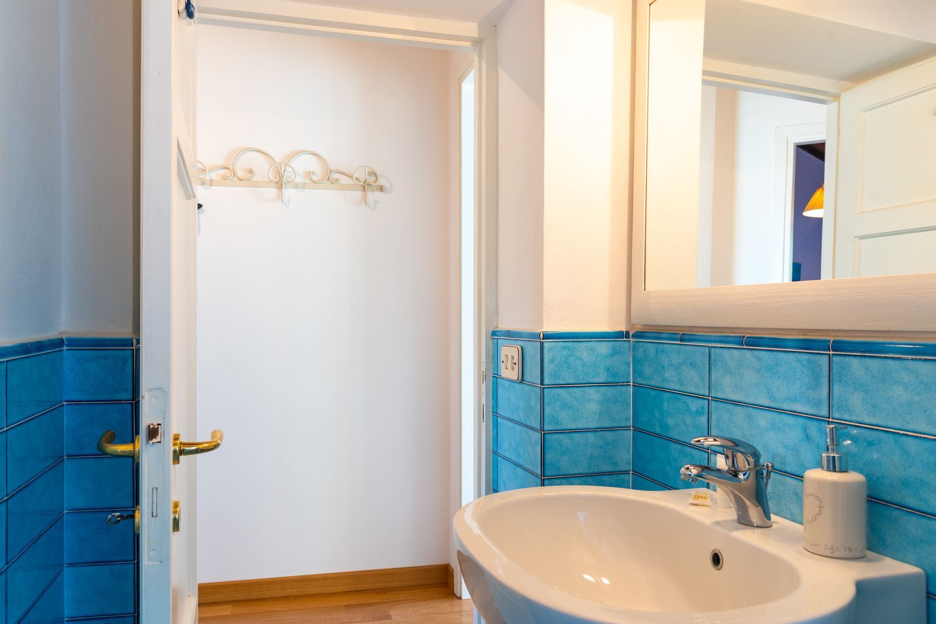 A bathroom with a white sink, blue tiles, a mirror, and a door with a metal handle.