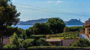 A coastal town with a prominent castle on a hill, lush greenery, and a clear view of the sea.