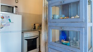 A kitchen with a white refrigerator, microwave, and stove. There is a blue cabinet with glass doors containing kitchenware.