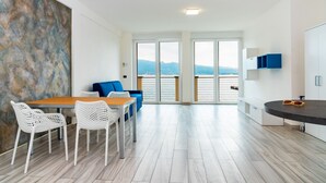 Une cuisine moderne avec un coin repas, des chaises blanches, un canapé bleu et une vue sur l’extérieur.
