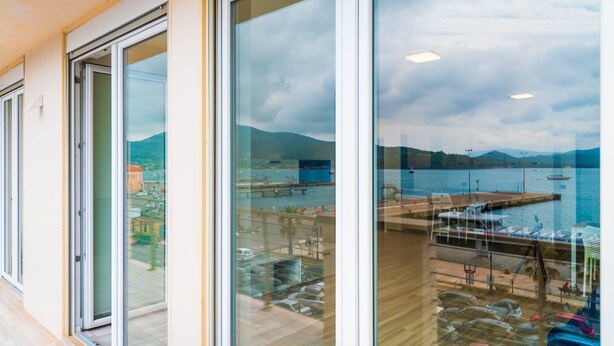 Un bâtiment moderne doté de grandes fenêtres en verre offrant une vue sur un port de plaisance et les montagnes.