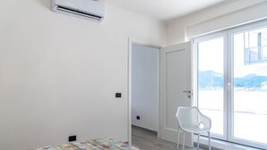 Een kamer met een bed, een airconditioner, een witte stoel en een deur die uitkomt op een balkon met uitzicht op bergen.