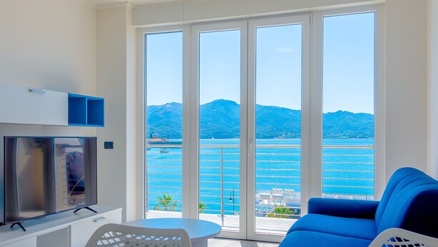 Ein Balkon mit Blick auf das Meer und die Berge, ein blaues Sofa, ein Fernseher und ein Tisch.