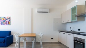 Eine moderne Küche mit weißen Schränken, einer schwarzen Arbeitsplatte und einem eingebauten Backofen. Es gibt einen Essbereich mit einem Holztisch und weißen Stühlen.