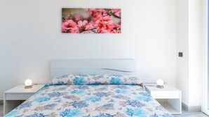 Ein Schlafzimmer mit einem Bett, zwei Nachttischen, einem Wandbild und einem Fenster.