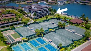 An aerial view of a tennis complex with multiple courts, surrounded by residential buildings and a body of water. - Bay view 1st floor condo with beach access. (Marco Island)
