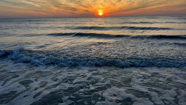 A sunset over the ocean with waves approaching the shore. - Bay view 1st floor condo with beach access. (Marco Island)