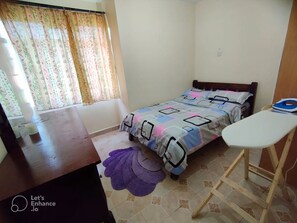 Cozy bedroom with a single bed, wooden desk, and ironing board.