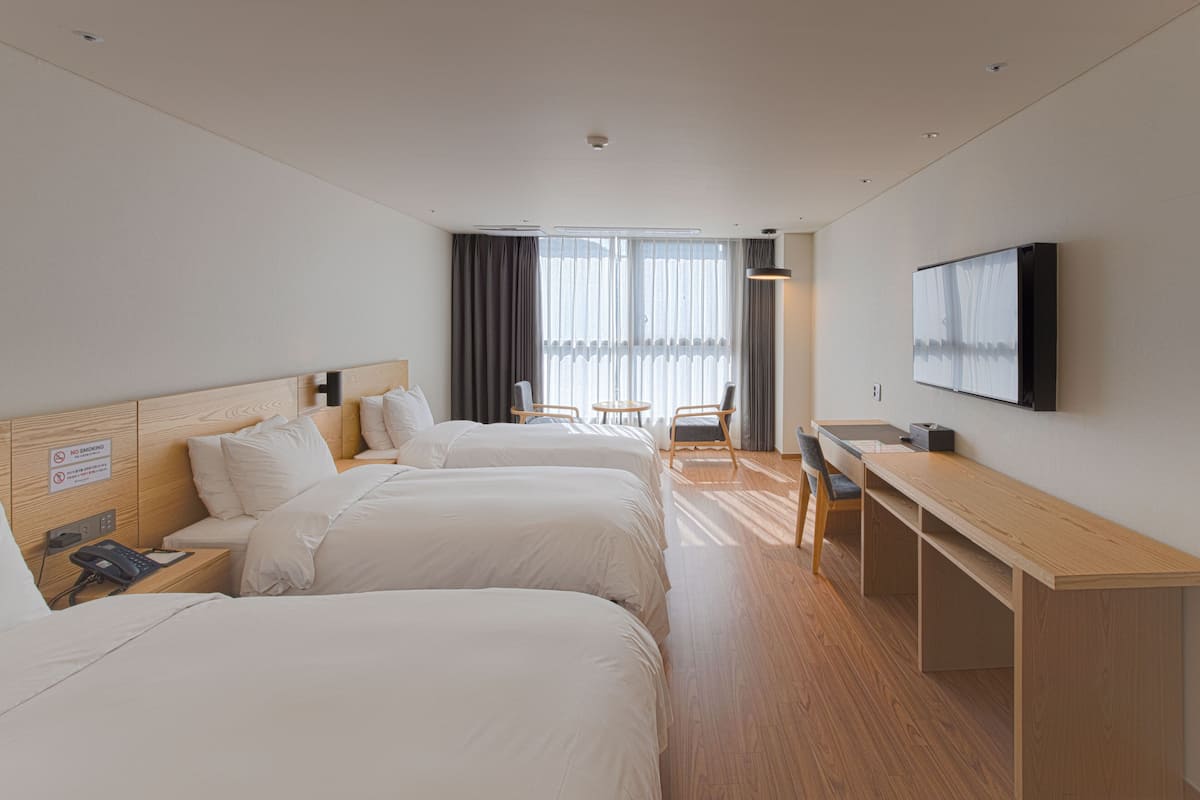 A hotel room with two beds, a desk, a chair, a TV, and a window with curtains.