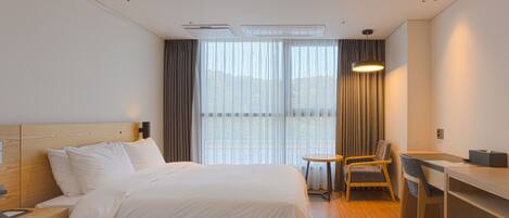 A hotel room with two beds, a desk, a chair, and a view of the outdoors.