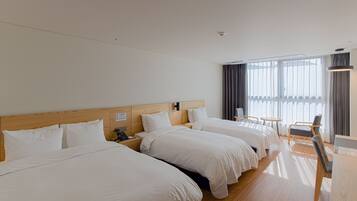 A hotel room with three beds, a wooden headboard, a desk, and a chair.
