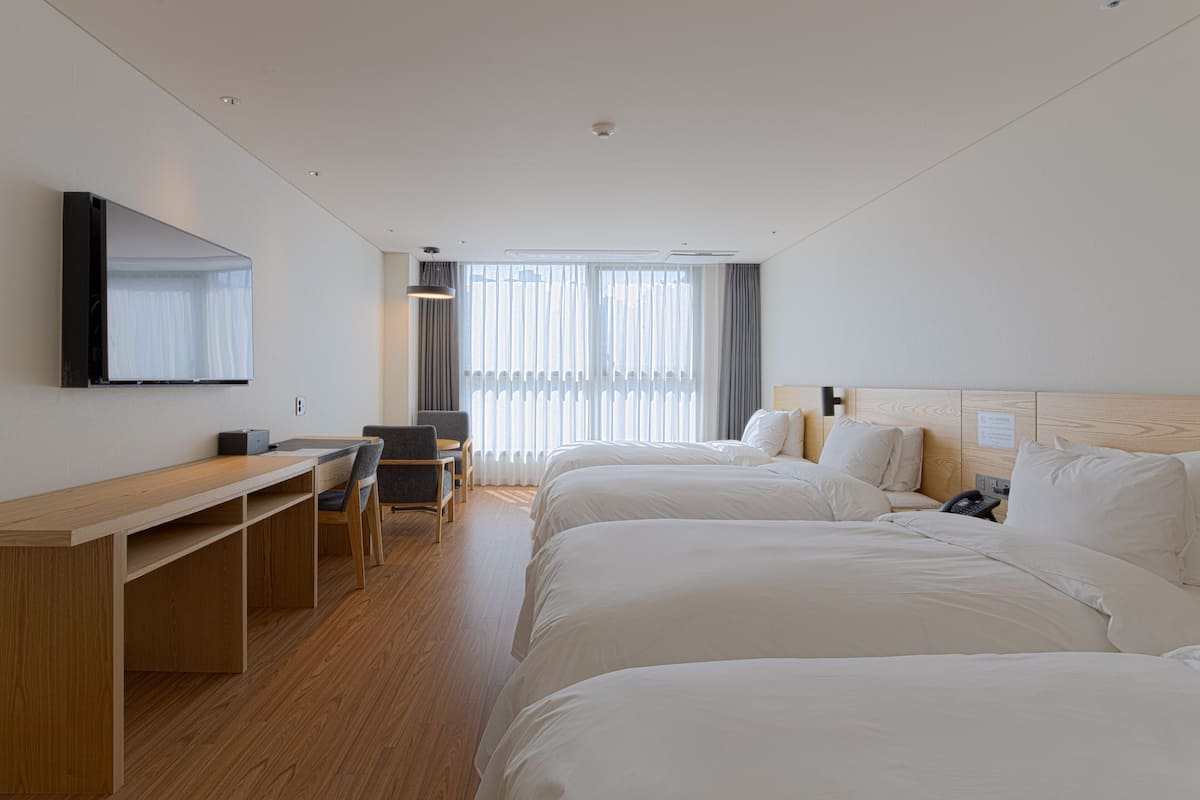 A hotel room with two beds, a desk, a chair, a TV mounted on the wall, and a window with curtains.