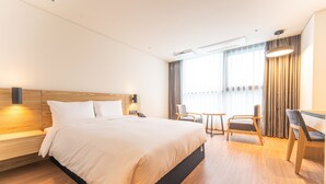 A hotel room with a large bed, a desk, two chairs, and a window with curtains. - Grand Moment (Busan)