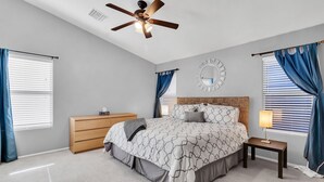 Un dormitorio con cama, cómoda, mesita de noche, ventilador de techo y un espejo en la pared.