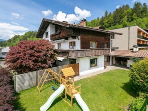 A two-story house with a wooden deck and a slide in the backyard.