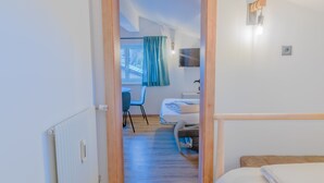 Un couloir étroit mène à une chambre qui contient un lit, un bureau et une chaise.