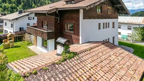 Une maison à deux étages avec un toit en pente, une terrasse en bois et un petit jardin.