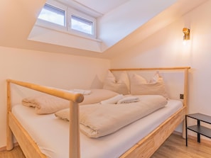 A single bed with a wooden frame and headboard, a small bedside table, and a skylight above.