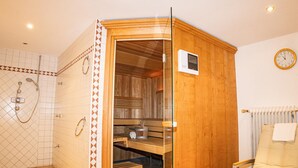 Un sauna avec une porte en bois, un banc et un espace douche doté d’une porte en verre.