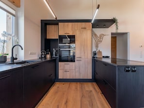 A modern kitchen with dark cabinetry, a wooden countertop, and a built-in oven.