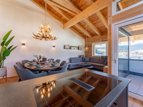 A modern kitchen with a central island, a dining area with a round table, and a living area with a sectional sofa.