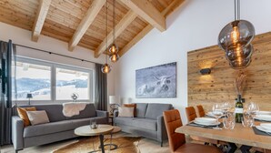 Un salon moderne avec un canapé, une table à manger et une grande fenêtre donnant sur des collines enneigées.